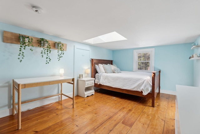 bedroom with light wood-style floors, a skylight, and baseboards