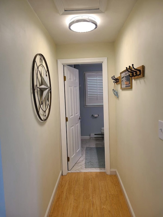 corridor with baseboard heating, light wood-style flooring, and baseboards