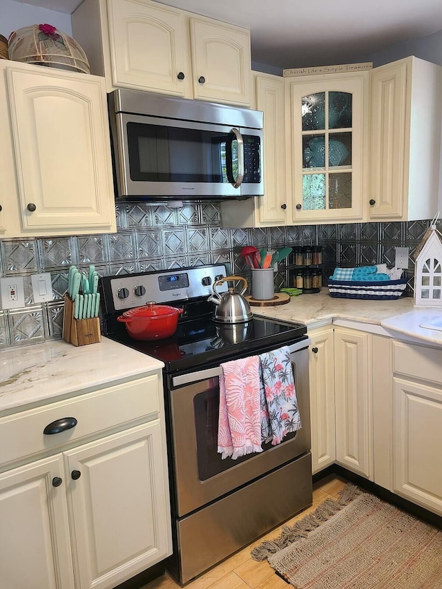 kitchen featuring glass insert cabinets, stainless steel appliances, backsplash, and light countertops