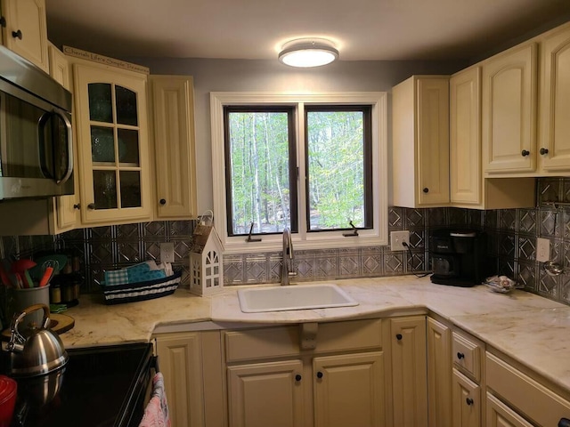 kitchen with stainless steel microwave, a sink, glass insert cabinets, and decorative backsplash