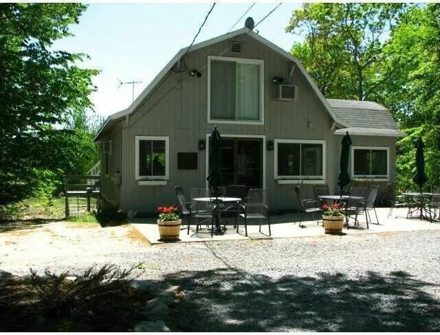 rear view of property featuring a wall mounted air conditioner, roof with shingles, a patio, and a gambrel roof