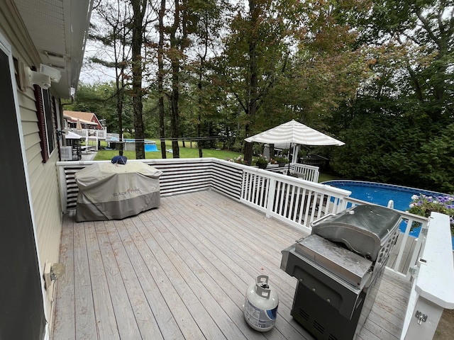 wooden terrace with an outdoor pool and area for grilling