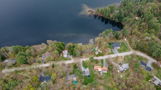 aerial view of property and surrounding area featuring a nearby body of water and a heavily wooded area