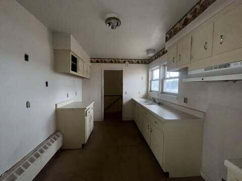 kitchen featuring light countertops, a baseboard heating unit, white cabinets, a sink, and under cabinet range hood