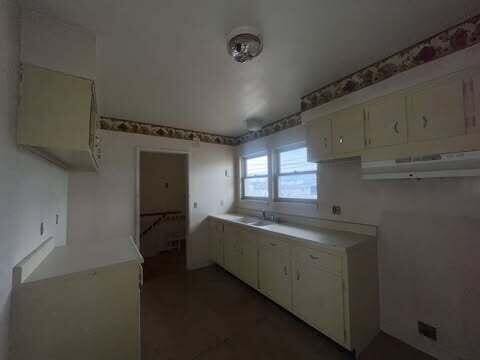 kitchen with light countertops, a sink, white cabinetry, and under cabinet range hood