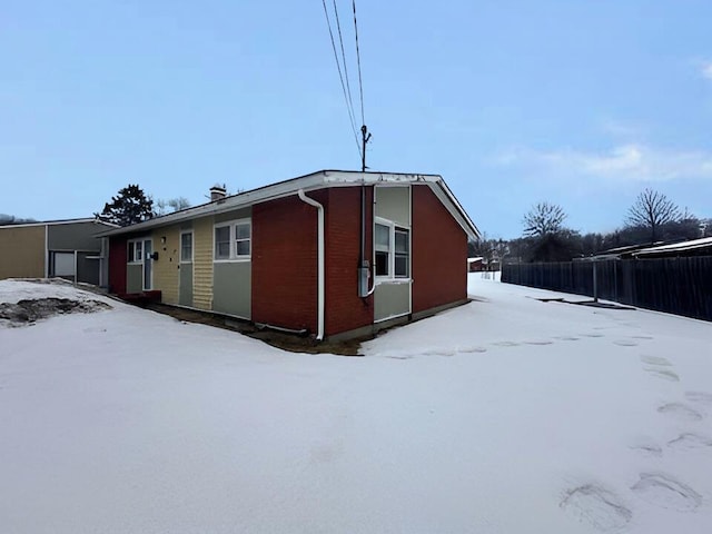 view of snow covered exterior featuring fence and brick siding