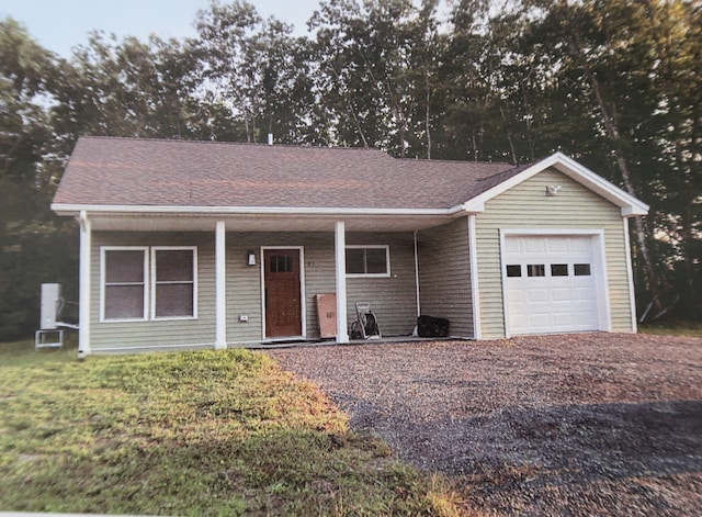 ranch-style house with a front yard, gravel driveway, roof with shingles, and an attached garage