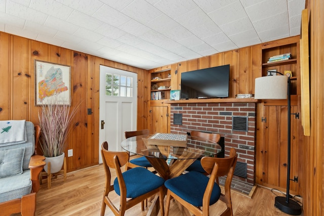 dining area with wood walls, light wood-type flooring, visible vents, and built in features