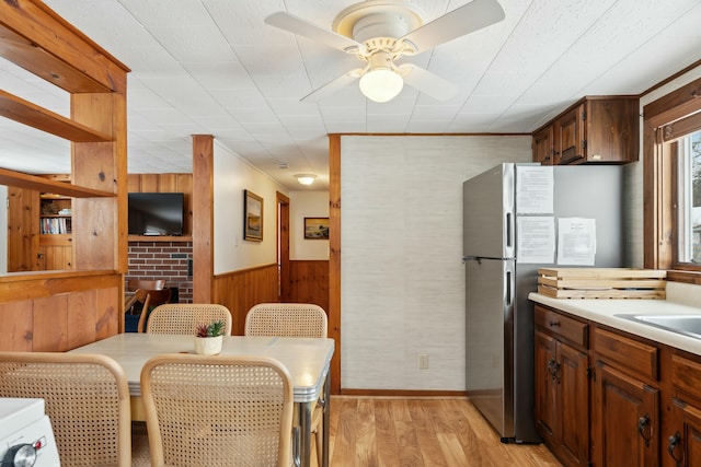 kitchen with wainscoting, freestanding refrigerator, light countertops, light wood-type flooring, and wood walls