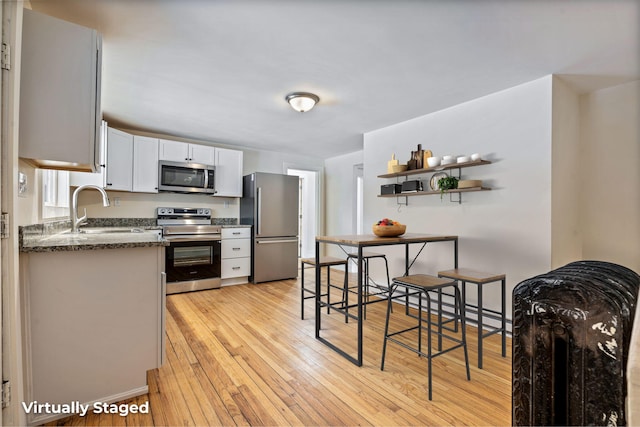 kitchen with stainless steel appliances, light wood-type flooring, white cabinetry, open shelves, and a sink