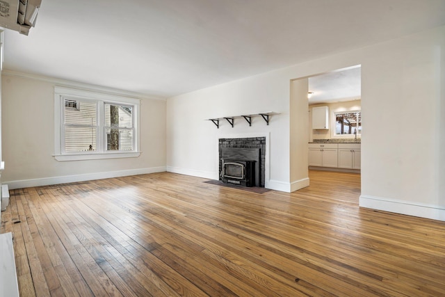 unfurnished living room featuring light wood finished floors, a wood stove, and baseboards