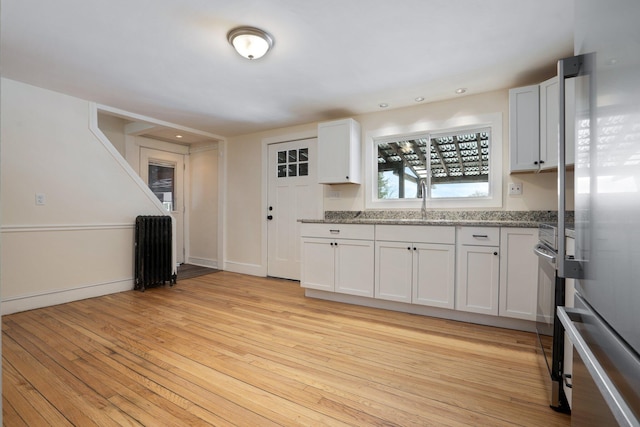 kitchen with light wood finished floors, appliances with stainless steel finishes, light stone counters, and white cabinets