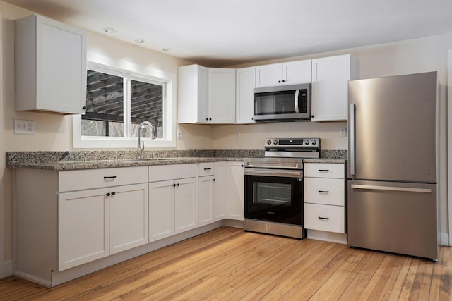 kitchen with light wood-type flooring, light stone countertops, white cabinetry, and stainless steel appliances