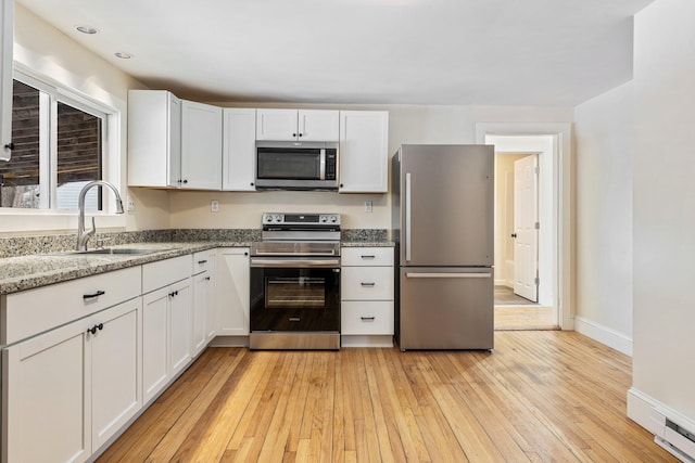 kitchen featuring white cabinets, light stone countertops, stainless steel appliances, light wood-style floors, and a sink