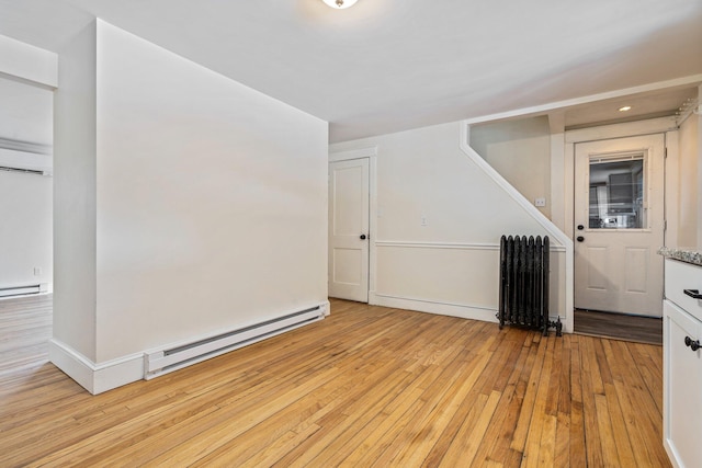 empty room with light wood-style floors, a baseboard radiator, baseboards, and radiator heating unit