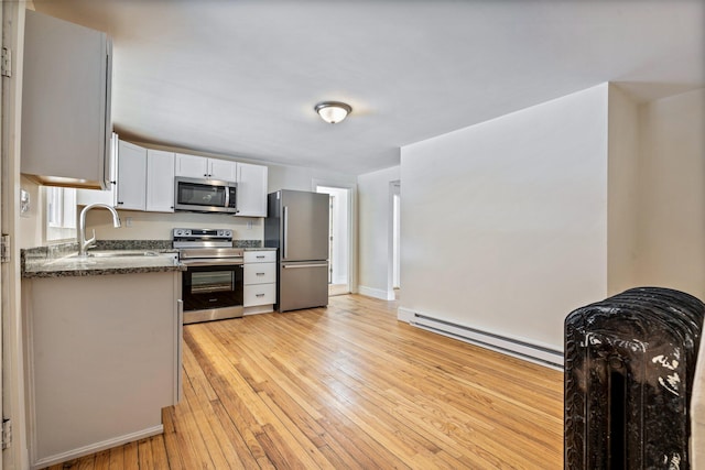 kitchen featuring baseboard heating, appliances with stainless steel finishes, light wood-style floors, white cabinets, and a sink