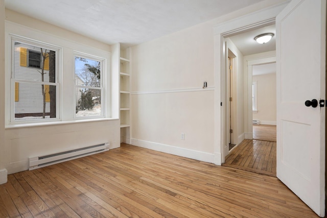 spare room with a baseboard heating unit, built in shelves, light wood-style flooring, and baseboards