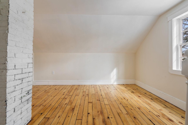 additional living space with light wood-type flooring, vaulted ceiling, and baseboards