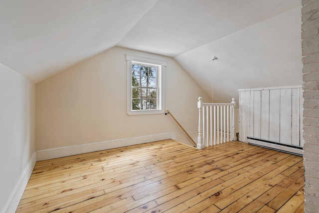 additional living space featuring a baseboard heating unit, vaulted ceiling, and light wood-style floors