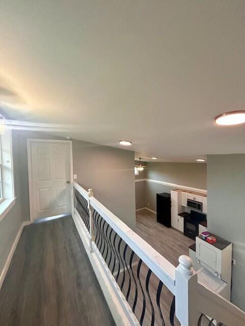 hall featuring lofted ceiling, baseboards, wood finished floors, and an upstairs landing