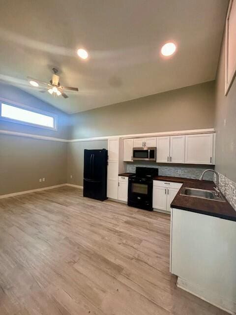 kitchen with a sink, white cabinets, black appliances, light wood finished floors, and dark countertops