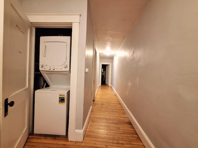 hallway featuring light wood-style floors, stacked washer / dryer, and baseboards