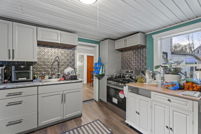 kitchen with a sink, light countertops, dark wood-style floors, tasteful backsplash, and stainless steel range with gas stovetop