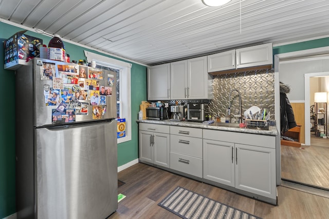 kitchen with a sink, appliances with stainless steel finishes, backsplash, light stone countertops, and dark wood finished floors