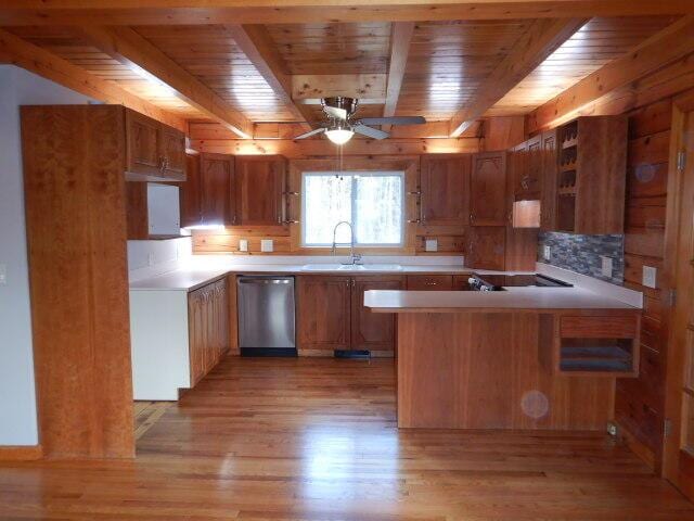 kitchen with a peninsula, a sink, light countertops, stainless steel dishwasher, and brown cabinetry