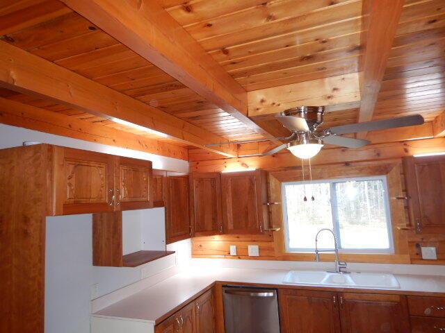 kitchen with a sink, light countertops, stainless steel dishwasher, beam ceiling, and brown cabinets