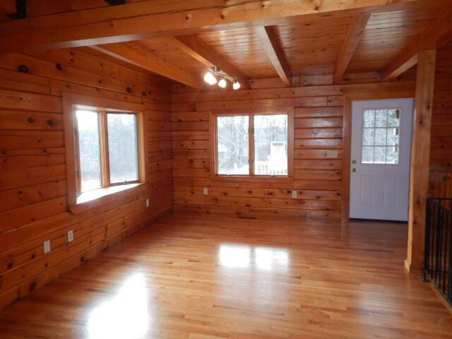 interior space with light wood-style floors, beam ceiling, and wood walls