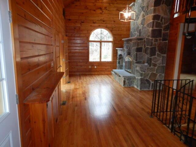 unfurnished living room featuring light wood-style floors, a fireplace, vaulted ceiling, and wood walls