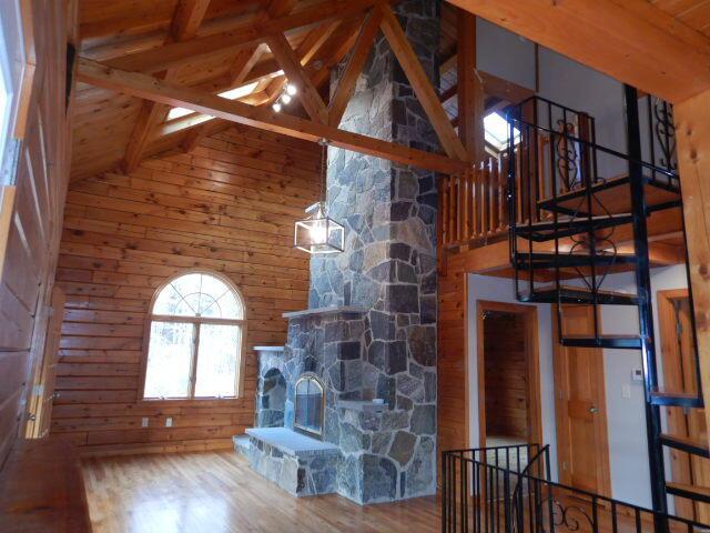 unfurnished living room with a fireplace, wood ceiling, wood walls, wood finished floors, and beamed ceiling