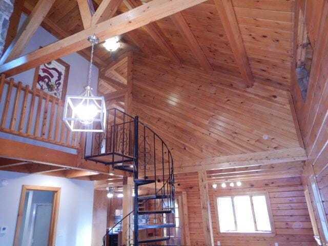 stairway featuring beam ceiling, a notable chandelier, wood ceiling, wood walls, and high vaulted ceiling