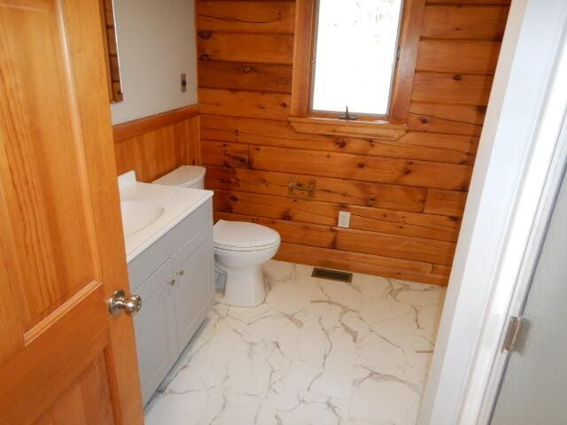 half bathroom featuring toilet, wooden walls, vanity, visible vents, and marble finish floor