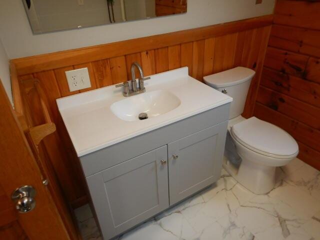 bathroom with marble finish floor, wainscoting, wooden walls, and vanity