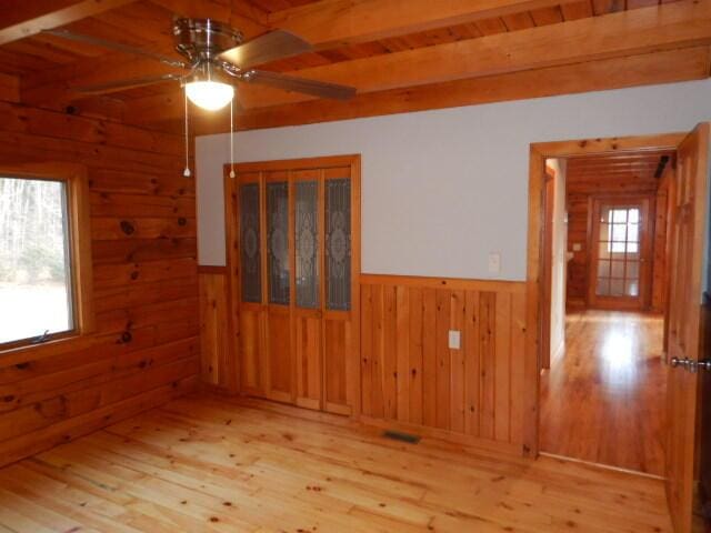 empty room with a wainscoted wall, light wood-style flooring, wooden walls, and beam ceiling