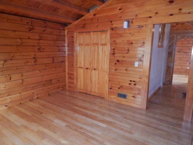 unfurnished room featuring vaulted ceiling with beams, light wood-type flooring, wood ceiling, and wooden walls