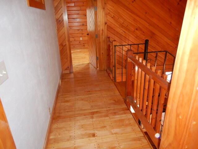 hall with an upstairs landing, wooden walls, and light wood finished floors