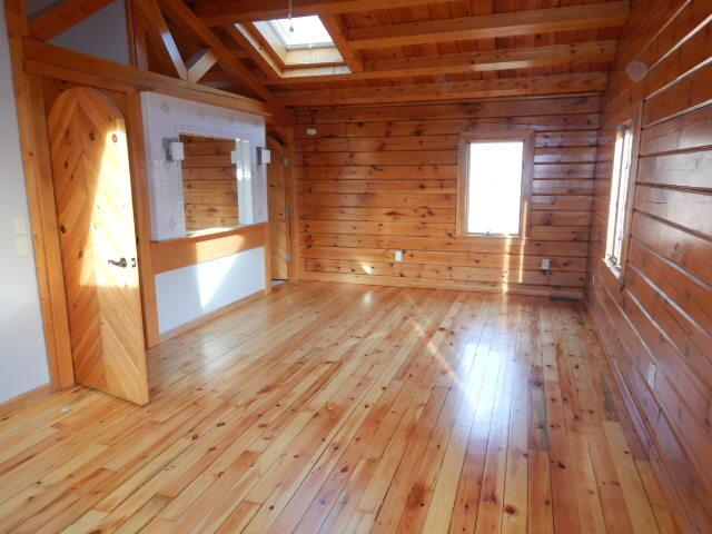 empty room with light wood finished floors, lofted ceiling with skylight, and wooden walls