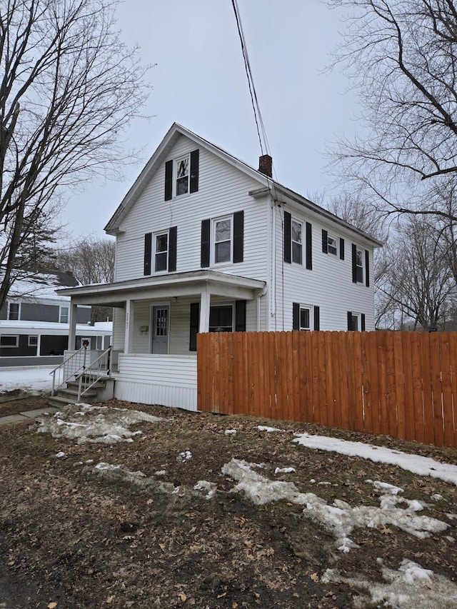 view of front of property featuring covered porch, a chimney, and fence