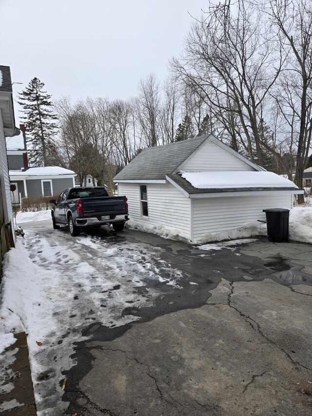 snow covered property with driveway and roof with shingles