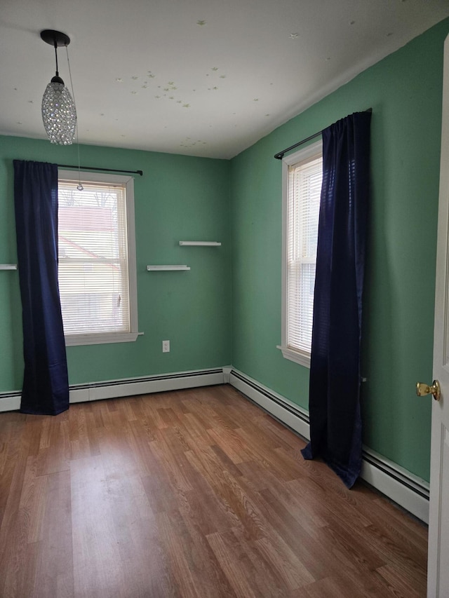 empty room with plenty of natural light, wood finished floors, and a baseboard radiator