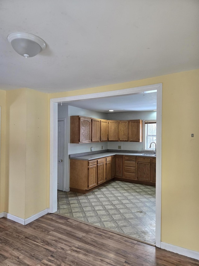 kitchen featuring light wood finished floors, baseboards, brown cabinetry, and a sink