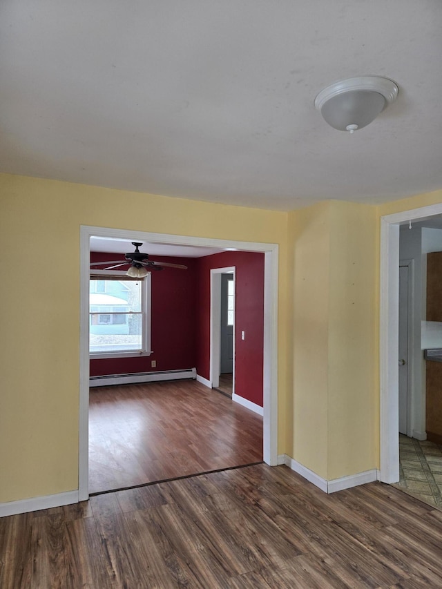 spare room featuring a baseboard heating unit, a ceiling fan, baseboards, and wood finished floors