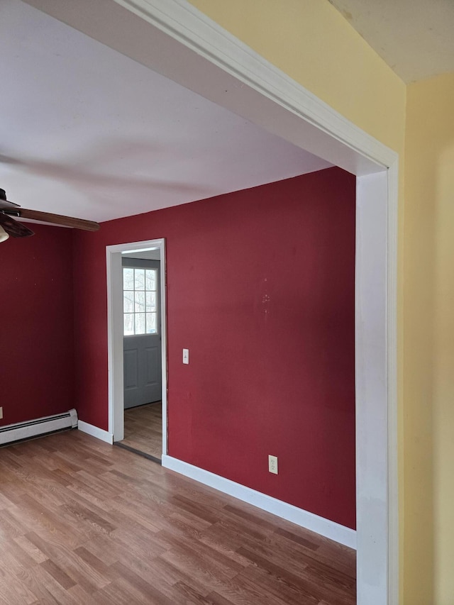 spare room featuring a baseboard radiator, wood finished floors, and baseboards