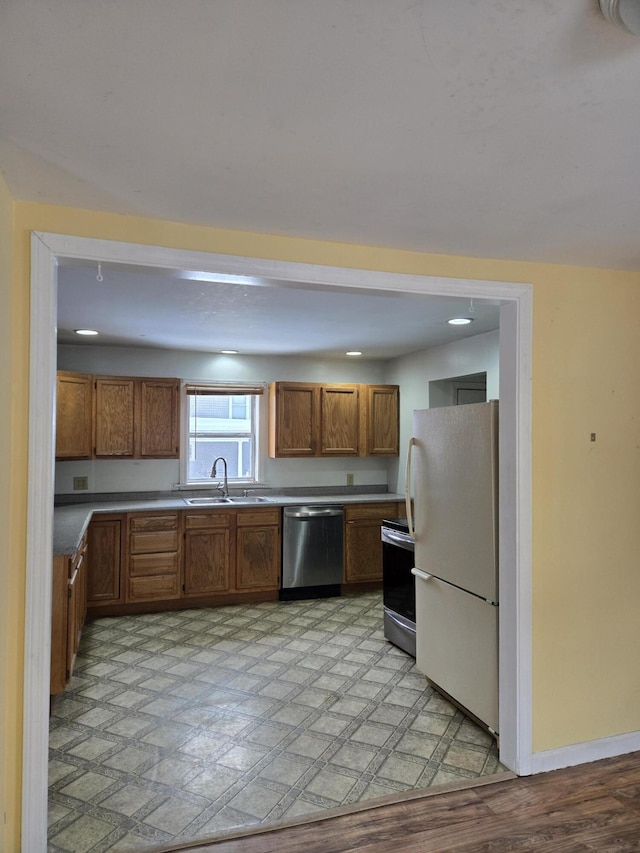 kitchen featuring baseboards, brown cabinetry, stainless steel appliances, light floors, and a sink