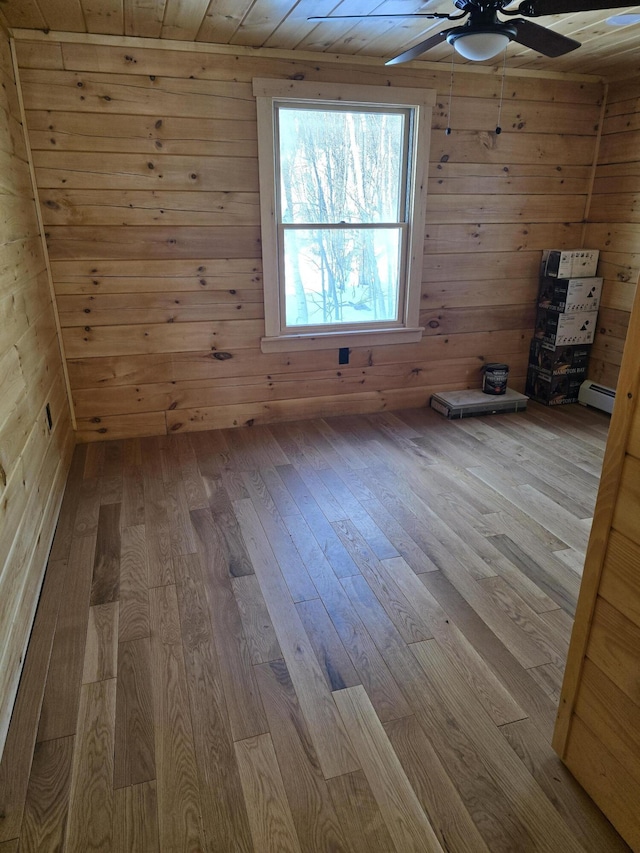 additional living space featuring a ceiling fan, a baseboard radiator, wood-type flooring, and wood walls