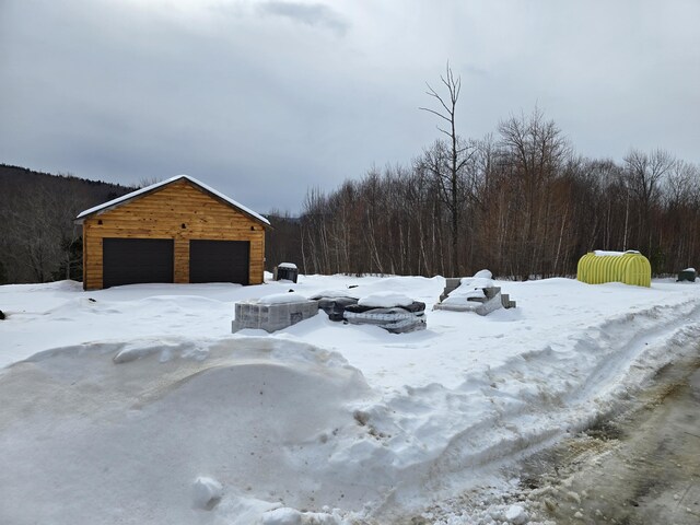 snowy yard featuring a forest view, a detached garage, and an outdoor structure