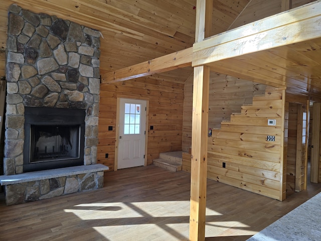 unfurnished living room with lofted ceiling, a fireplace, wood finished floors, and wooden walls